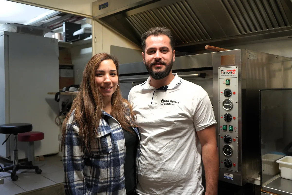 Man sieht einen Mann und eine Frau vor einem Pizzaofen.